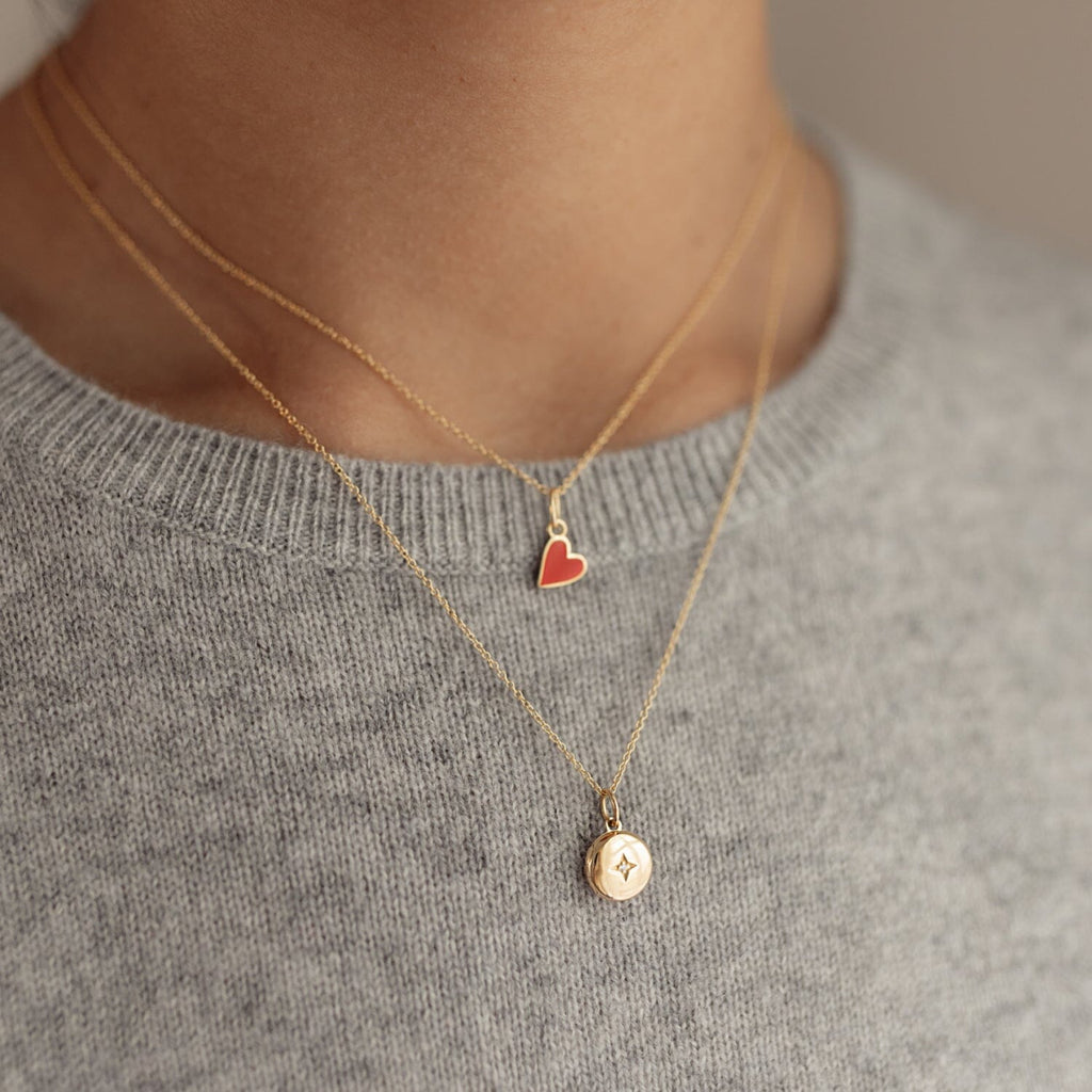 woman wearing gray sweater with red enamel heart necklace and round mini locket