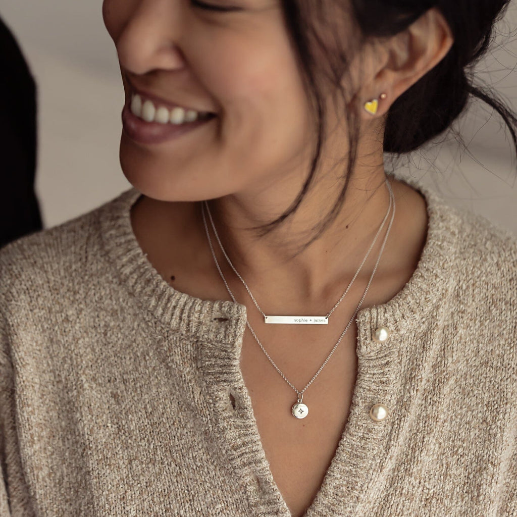 Woman wearing Tiny Tags skinny bar necklace and round mini locket