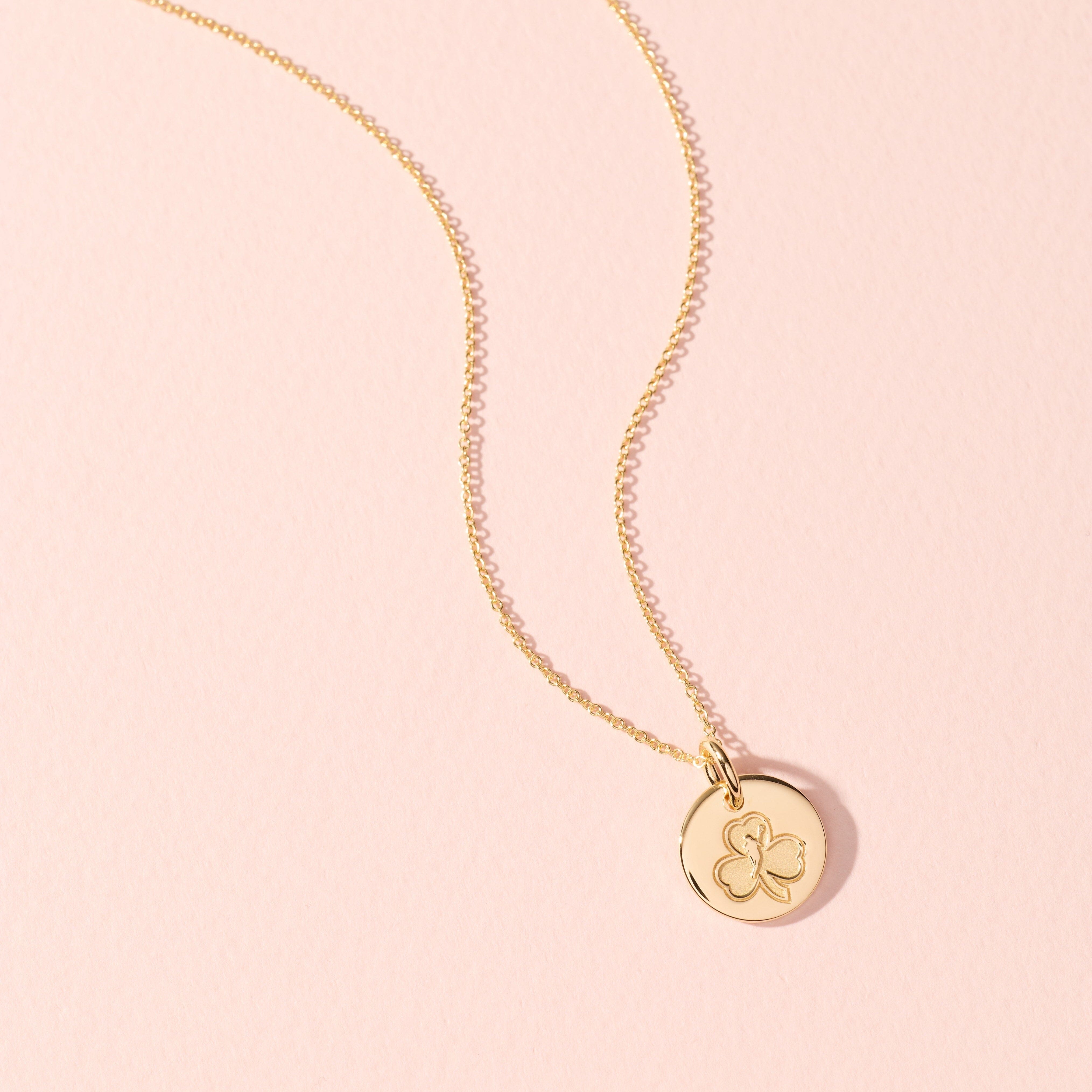 Gold necklace with a round pendant on a pink background