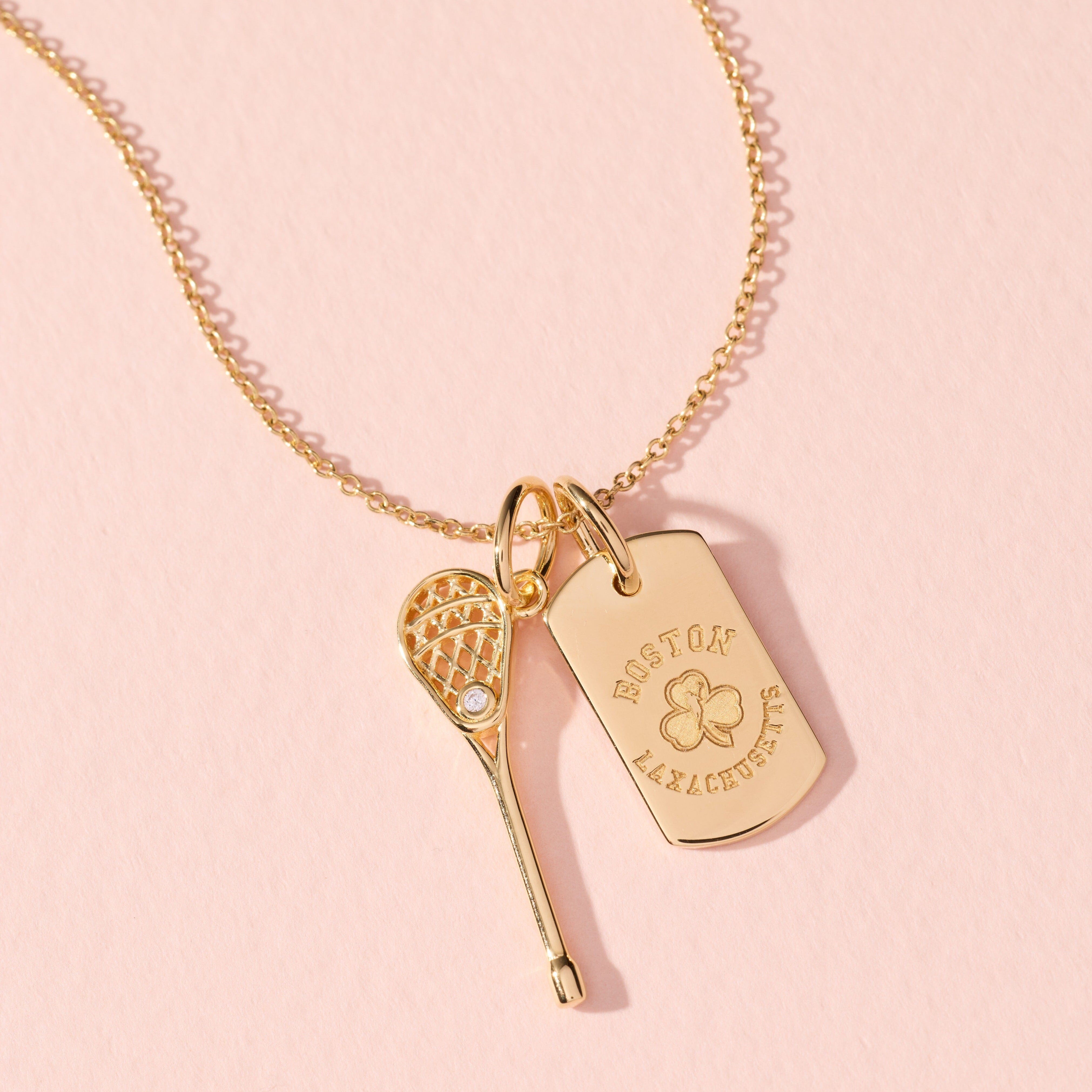 Gold necklace with heart, tennis racket, and tag pendant on a pink background