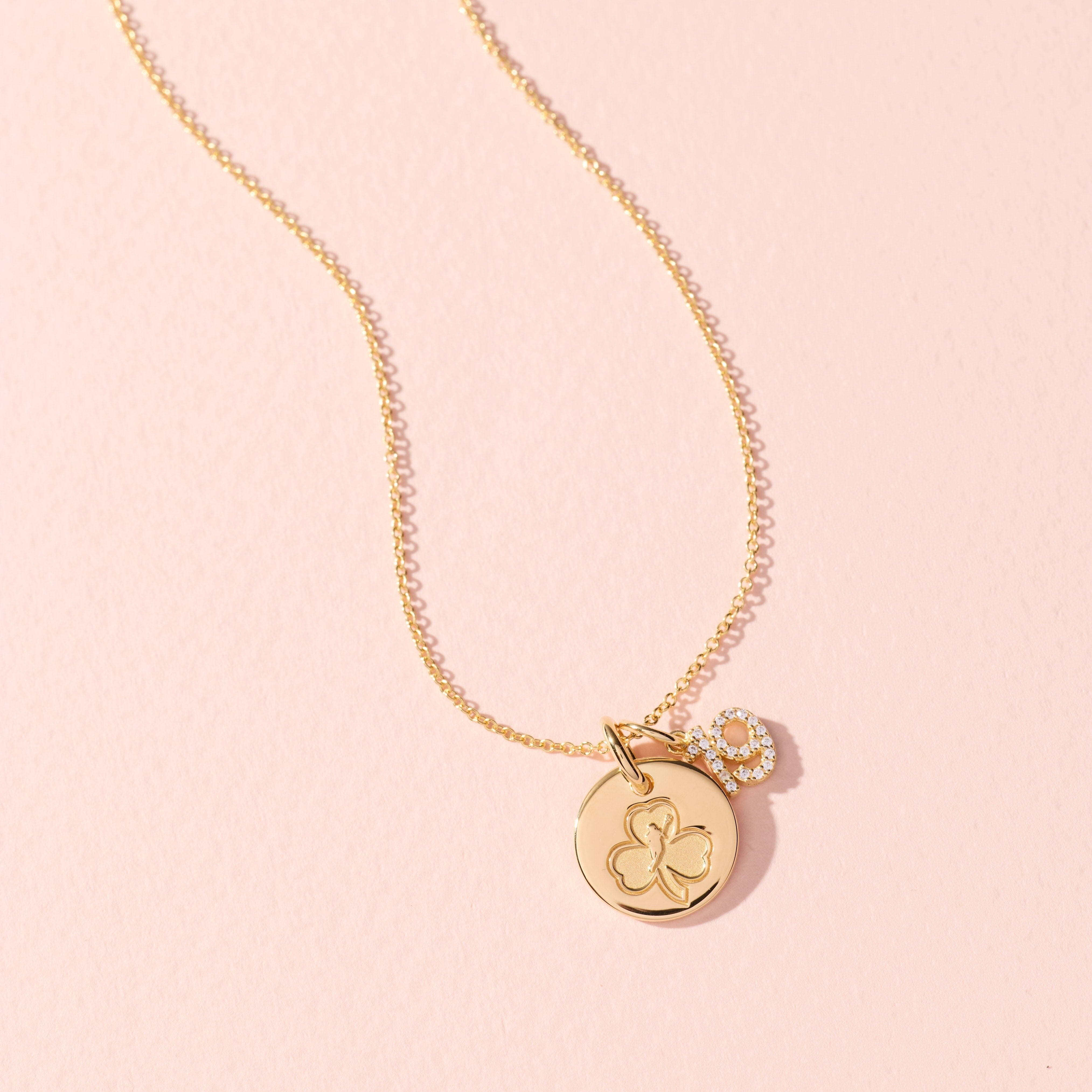 Gold necklace with a round pendant on a pink background