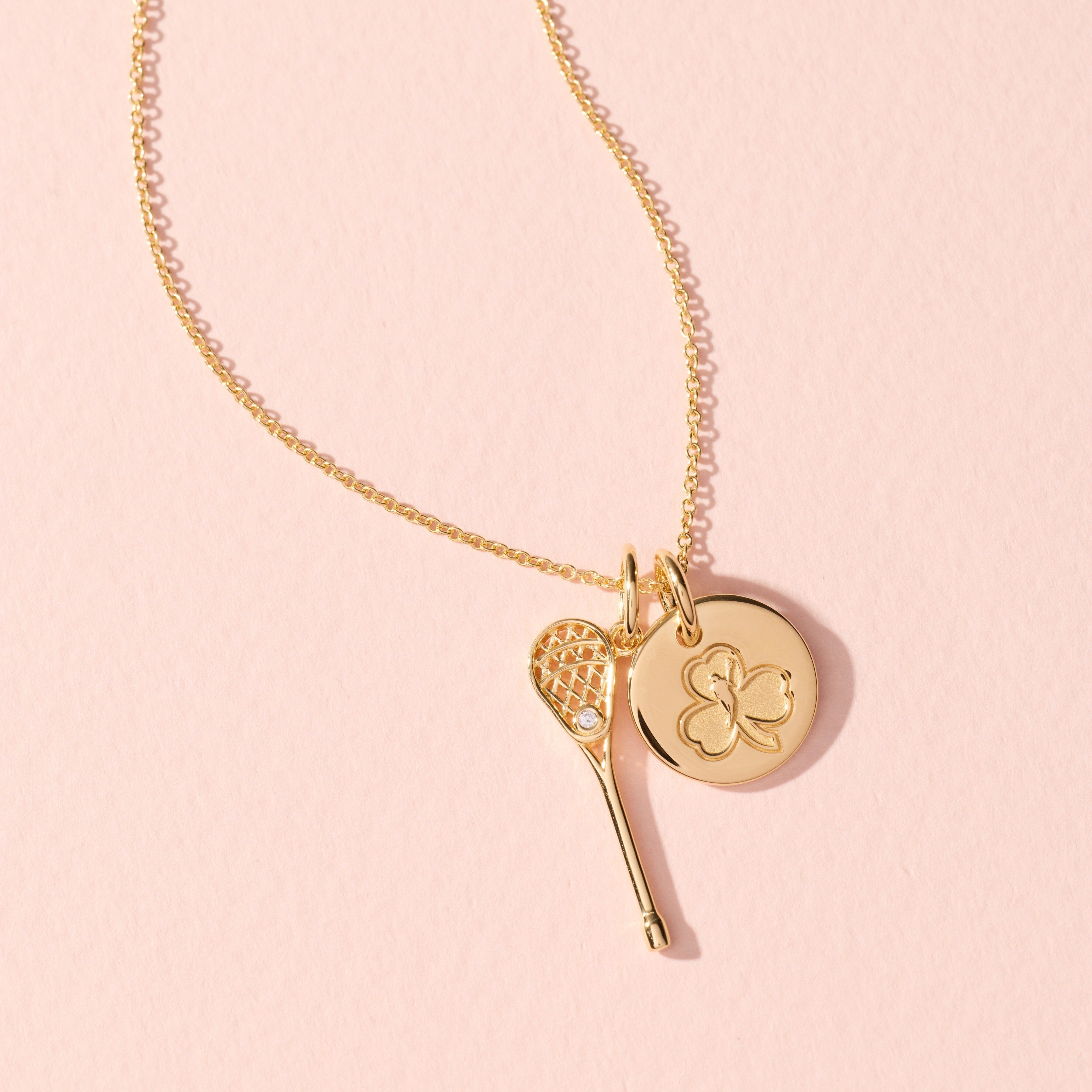 Gold necklace with key and round pendant on a pink background