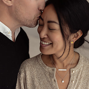 Woman getting a kiss from a man while wearing two Tiny Tags necklaces