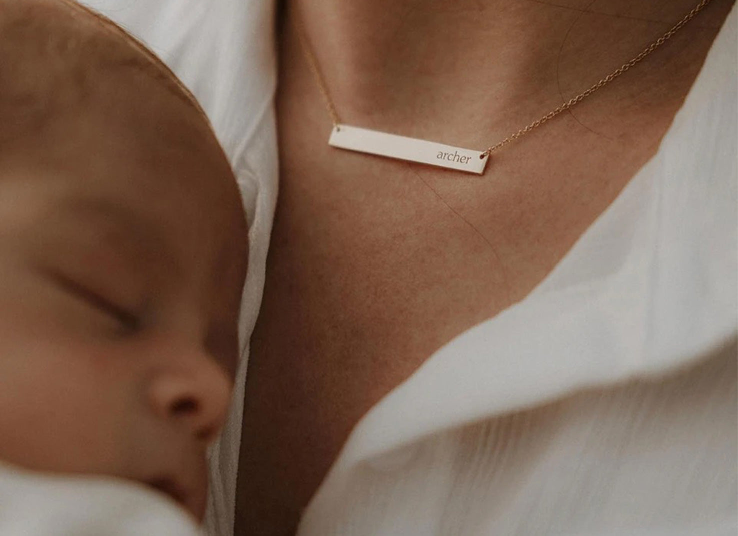 close up of woman holding a baby and wearing a skinny bar necklace